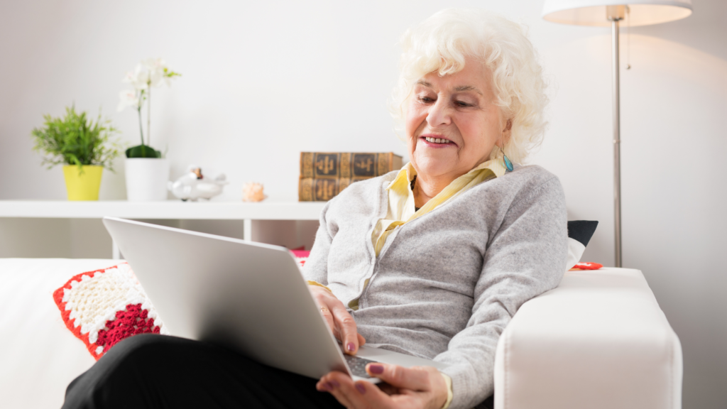 an elderly woman holding a laptop to video call family to 